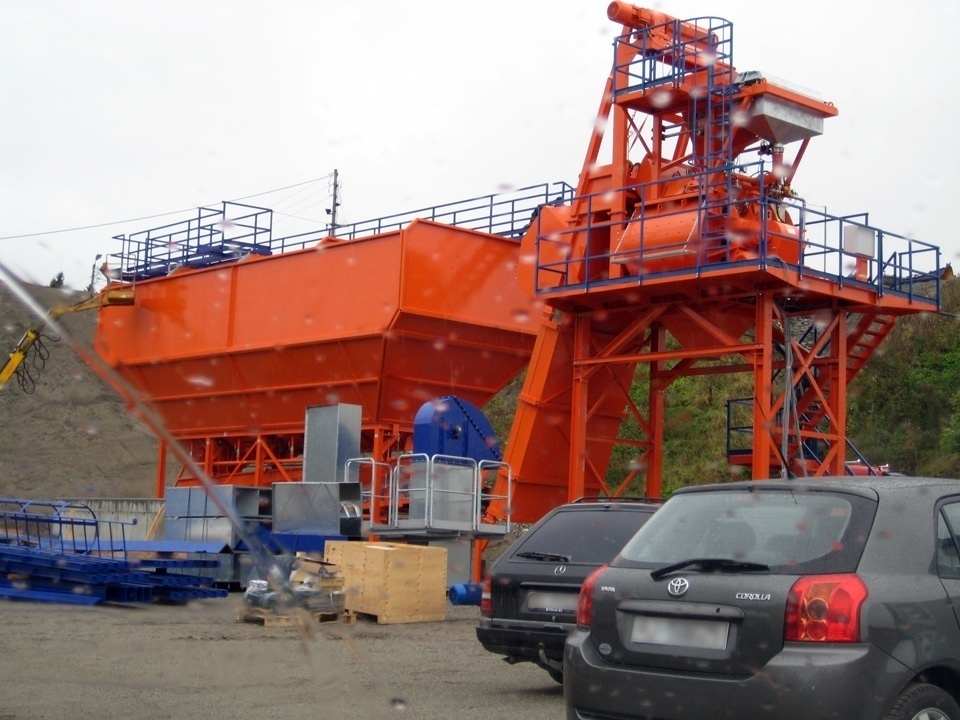 Tecwill preassembled concrete batching plant installed on site, featuring an orange modular structure, aggregate storage unit, and elevated mixing tower.
